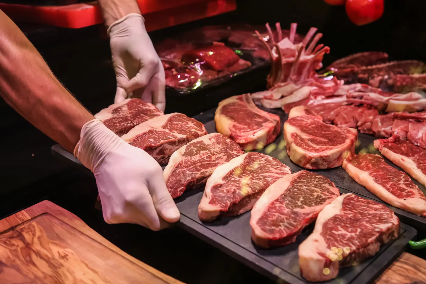 Manos con guantes acomodando bifes sobre una bandeja de pizarra